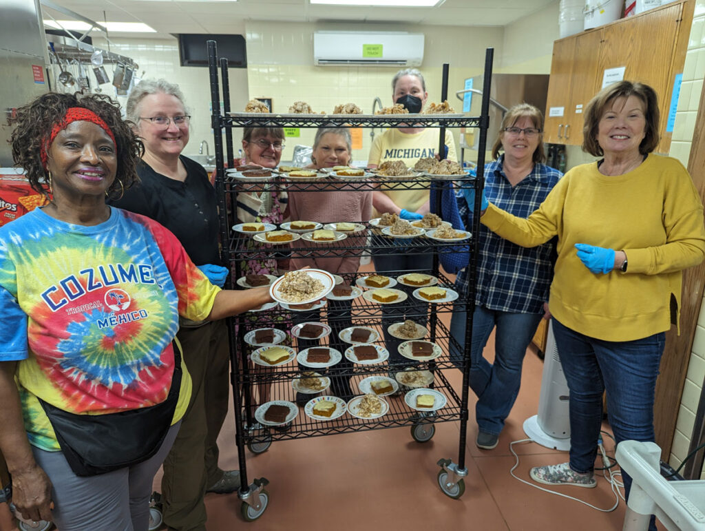 Volunteers at Foot at First, Ames standing around a tall multi-level rack with various desserts.